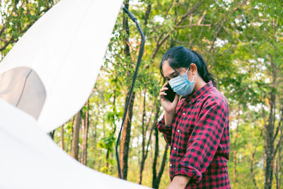 Portrait of young woman photographing against trees