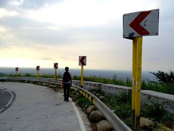 Road sign on road against cloudy sky