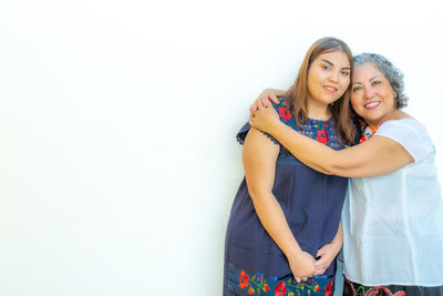 Portrait of a mother hugging her daughter with lots of love, standing against a white background