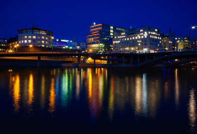 Illuminated bridge over river by buildings against sky at night