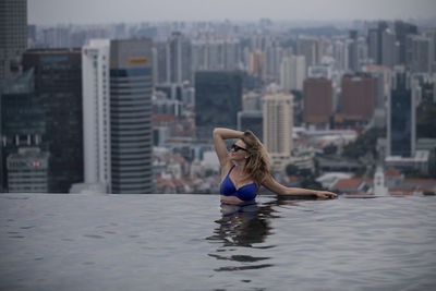 Woman relaxing in swimming pool against buildings in city