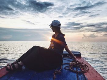 Man sitting on beach against sky during sunset