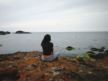 Woman sitting at beach against sky