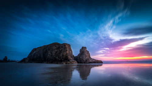 Rock formation in sea against sky during sunset