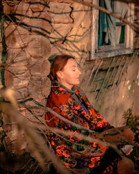 Portrait of ukrainian woman in a colorful knitted scarf near wooden house on a summer evening 