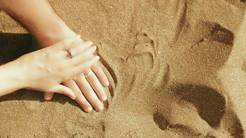 Cropped image of hands with wedding rings on sand