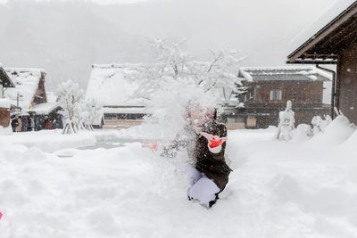 Snow covered houses by building during winter