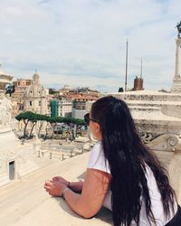 Side view of woman sitting against buildings in city