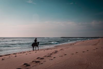 People riding horse on beach against sky