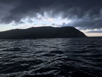 Scenic view of sea and mountains against storm clouds