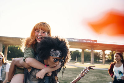 Young man piggybacking happy friend while enjoying in music festival