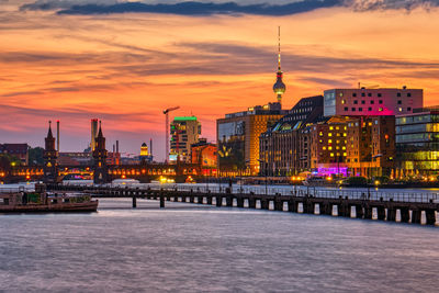 Illuminated buildings at waterfront during sunset