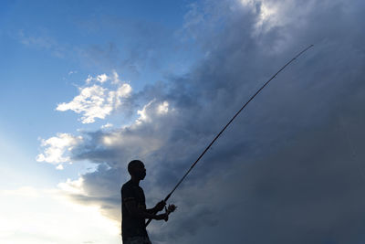 Low angle view of silhouette man fishing against sky