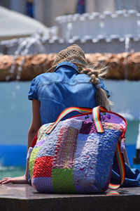 Rear view of woman sitting on retaining wall of fountain