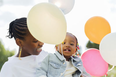 Young woman carrying cute daughter holding balloons at park