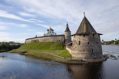 View of castle by river against cloudy sky