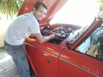 Portrait of smiling young man repairing red car