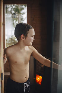 Smiling shirtless boy standing at doorway of sauna