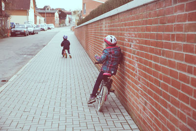 Children riding bicycle on sidewalk by brick wall