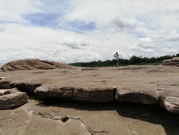 Rear view of man standing on rock against sky