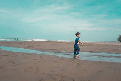 Rear view of boy running at beach against sky