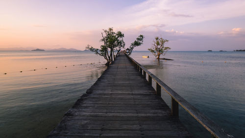 Scenic view of long wooden bridge over peaceful water in sunset orange sky. koh mak island, thailand