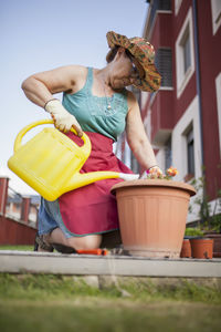 From below mature woman watering flowers on a sunny day