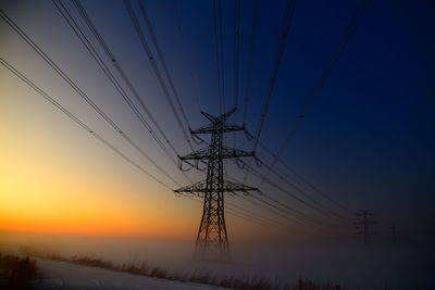 Low angle view of electricity pylon against sky during sunset, standing in a foggy ground