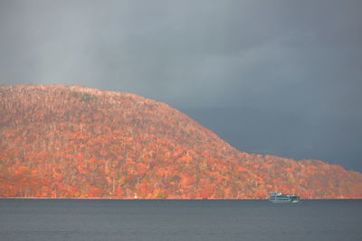 Scenic view of sea by mountain against sky