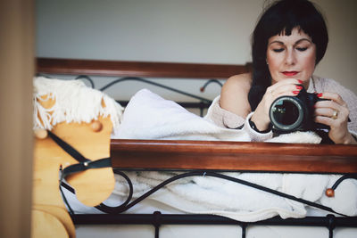 Woman photographing while lying on bed at home