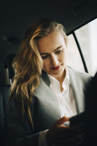 Businesswoman using internet through smart phone while sitting in taxi during business trip