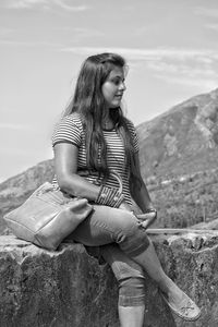 Woman sitting on retaining wall against sky