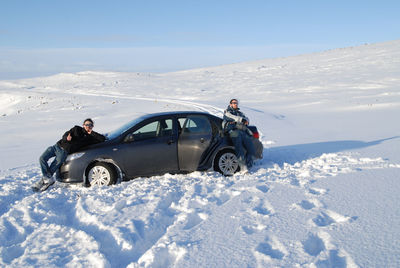 Male friends standing by car on snow covered field