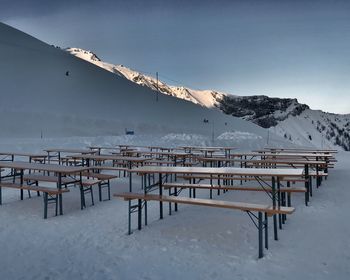 Empty tables and seats on snowcapped mountain against clear blue sky