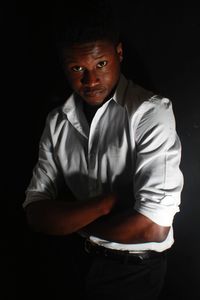 Portrait of young man with arms crossed standing against black background