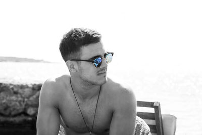 Handsome shirtless man wearing sunglasses at beach against clear sky