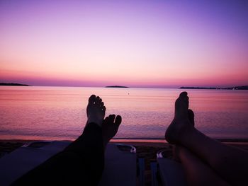 Low section of person in sea against sky during sunset