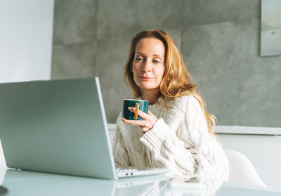 Young adult forty years woman with long hair working on laptop sitting on kitchen at home