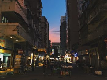 People walking on illuminated street amidst buildings in city at dusk