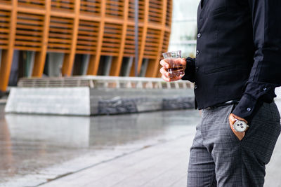 Midsection of man holding drink standing against glass