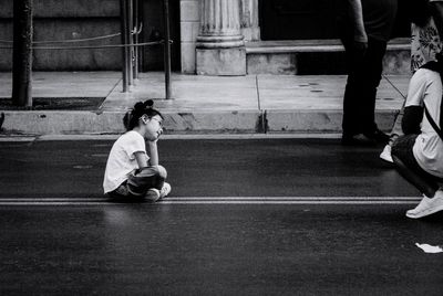 Side view of girl sitting on road in city