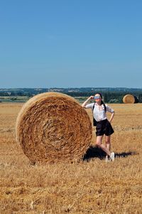 Woman standing by hay bale on land