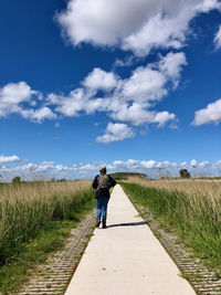 Rear view of man walking on road amidst field against sky