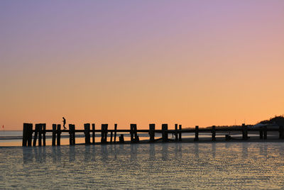 Silhouette pier on sea against clear sky during sunset