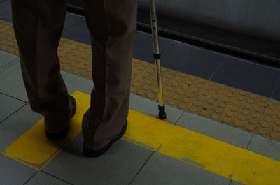 Low section of man standing with walking cane on railroad station platform