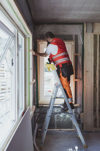 Full length of male construction worker standing on step ladder working at site