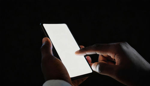 Cropped hand of person using mobile phone against black background