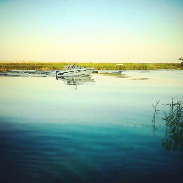 clear sky, water, copy space, tranquil scene, tranquility, lake, scenics, nature, reflection, beauty in nature, waterfront, river, calm, blue, landscape, idyllic, outdoors, no people, transportation, grass