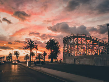 Silhouette palm trees and amusement park against sky during sunset