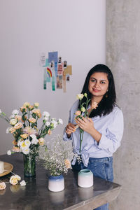 Florist of indian ethnicity looking at camera, smiling while she makes a flower arrangement 